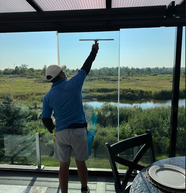 Technician with squeegee in glass room overlooking river